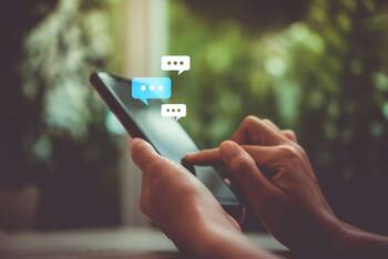 Zwei Hände tippen auf Smartphone mit virtuellen Chat-Textblasen als Hologramm um das Smartphone herum