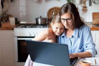 Frau und Kind sitzen in Küche vor Laptop und schauen gemeinsam auf Bildschirm