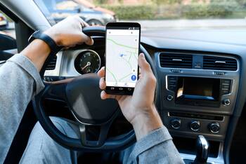 Mann fährt Auto mit Smartphone mit geöffneter Navigationsapp in der Hand