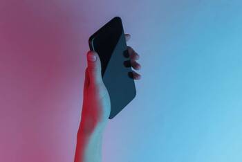 schwarzes Smartphone wird vor blurotem Hintergrund gehalten