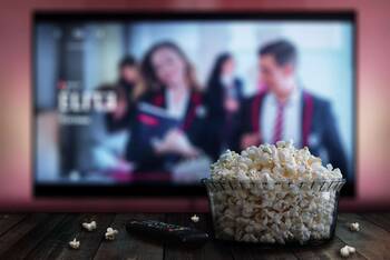 Fernseher mit Netflix im Hintergrund, im Vordergrund sind Popcorn und Fernbedienung