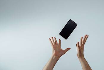 Handy wird von zwei Händen vor neutralem Hintergrund in die Luft geworfen