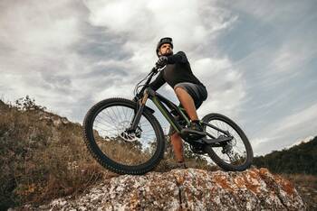 Mann steht mit Fahrrad auf einem Hang