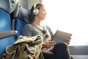 Frau sitzt mit Kopfhörern und Tablet im Zug 