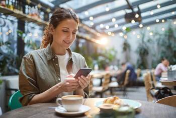Frau sitzt in Café und schaut auf Smartphone