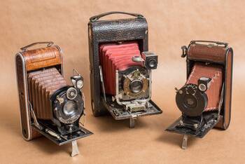Drei Oldtimer Fotokameras auf einem beigen Hintergrund.