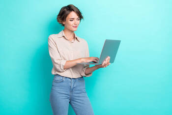 Frau steht mit Laptop in der Hand vor türkisem Hintergrund