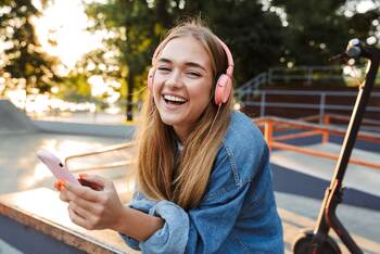 Jugendliche mit Kopfhörern und Smartphone in den Händen schaut lächelnd in die Kamera
