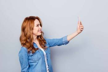 Eine Frau hält ein Smartphone in der Hand und macht ein Foto von sich selbst.