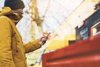 Mann mit Winterjacke und Mütze bedient Smartphone