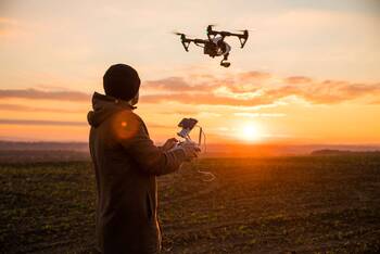 Person steuert Drohne mithilfe einer Fernbedienung auf Feld bei Sonnenuntergang