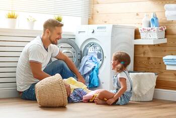 Mann und und Kinde sitzen mit Wäsche vor Waschmaschine