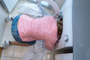 Frau kniet vor einer Waschmaschine mit ihrem Kopf in der Trommel