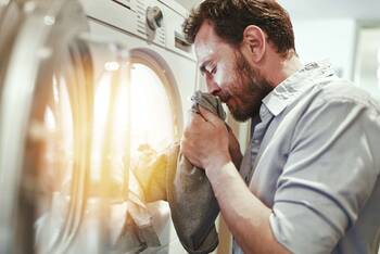Mann riecht an der Wäsche aus der Waschmaschine