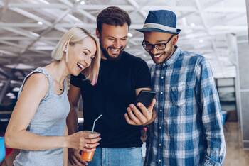 Drei Leute schauen fröhlich auf ein Smartphone