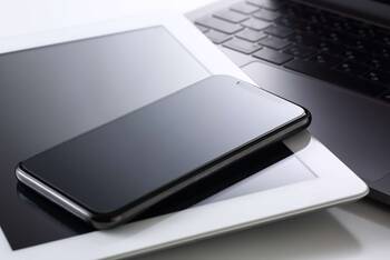 Smartphone liegt auf Tablet, welches auf einer Laptop-Tastatur liegt