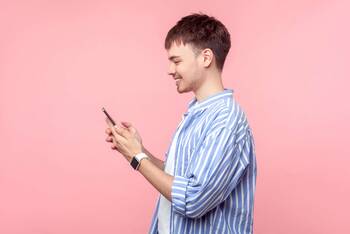 Mann steht vor einem pinken Hintergrund und lächelt auf sein Smartphone