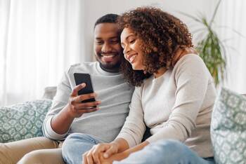 Zwei Personen auf einer Couch schauen lächelnd auf Smartphone