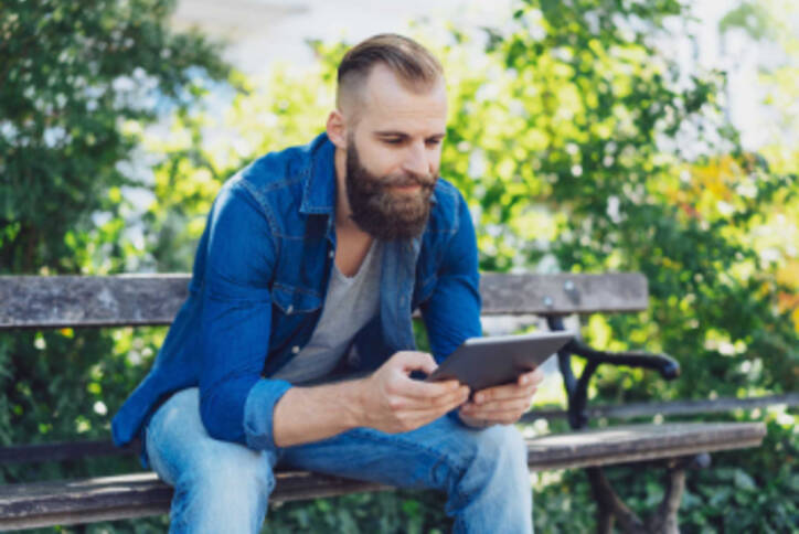 Mann sitzt mit Tablet auf Parkbank