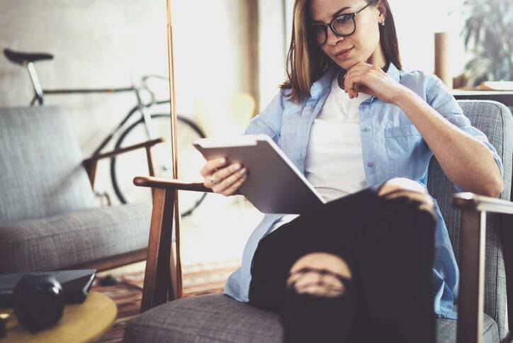 Frau in modernem Umfeld mit Jeanshemd hält iPad in der Hand