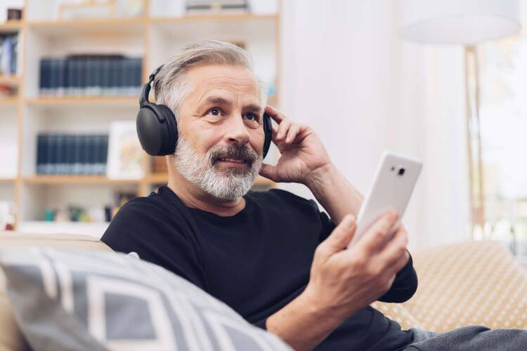 Mann mit Over Ear Kopfhörern hält Smartphone in der Hand