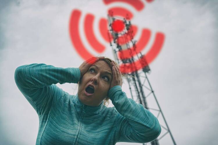 Frau hält sich am Kopf vor Funkmast mit Strahlensymbol