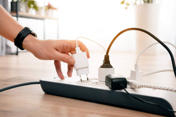 Einer Person steckt ein Netzteil in einer Steckerleiste. 