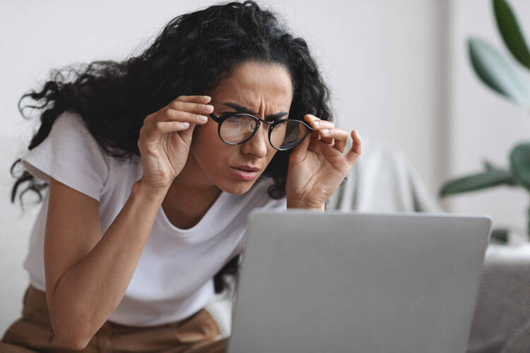 Eine Frau blickt fragend auf ihren Laptop. 