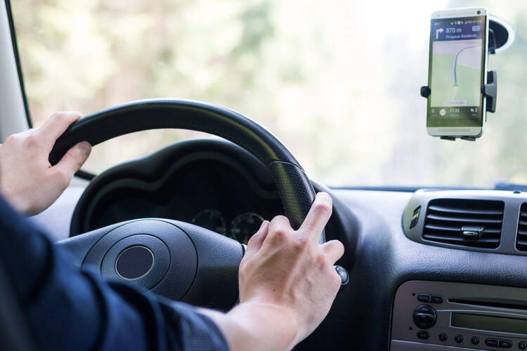 Eine Person hat ein Handy mit einem Navigationsdienst geöffnet und fährt Auto.