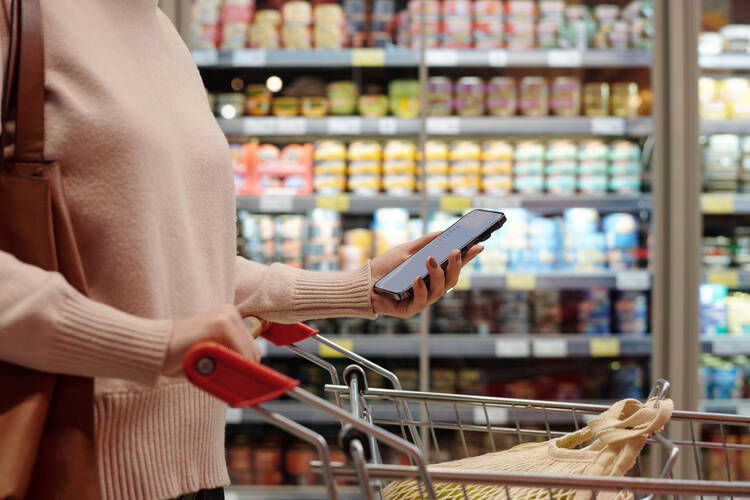 Eine Frau blickt beim Einkauf im Supermarkt auf ihr Smartphone.