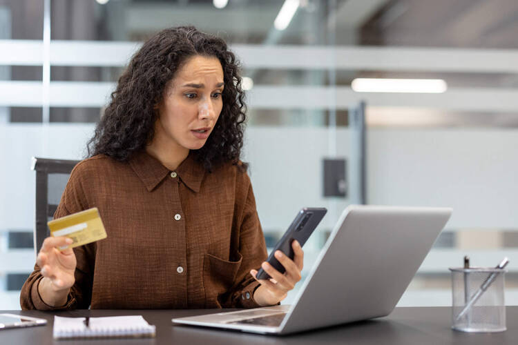 Eine Frau sitzt fassungslos vor dem Laptop. während sie ihre Bankkarte in der Hand hält.