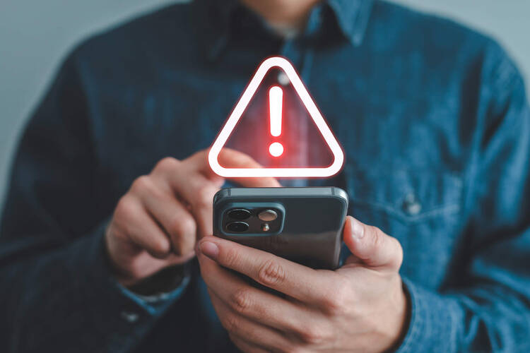 Ein Mann hält ein Smartphone in der Hand, das ein Warnsignal anzeigt.