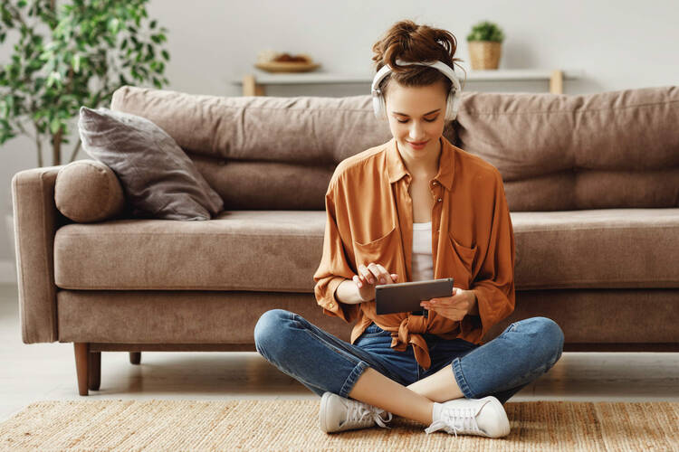 Eine Frau sitzt auf dem Boden vor ihrem Sofa und schaut auf ihr Tablet.