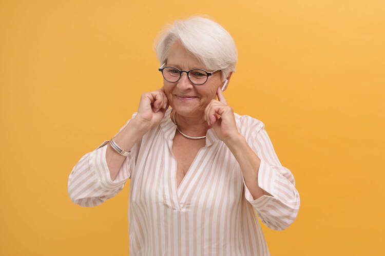 Eine ältere Frau hat AirPods im Ohr. 