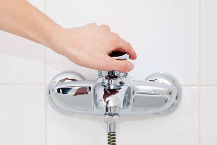 Eine Person dreht an dem Wasserventil der Badewanne.