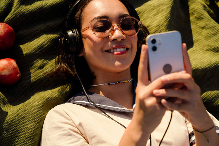 Eine Frau liegt auf einer Decke in der Sonne und hört über ihre Kopfhörer Musik.