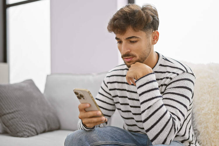 Ein Mann sitzt auf dem Sofa und blickt in sein Smartphone.