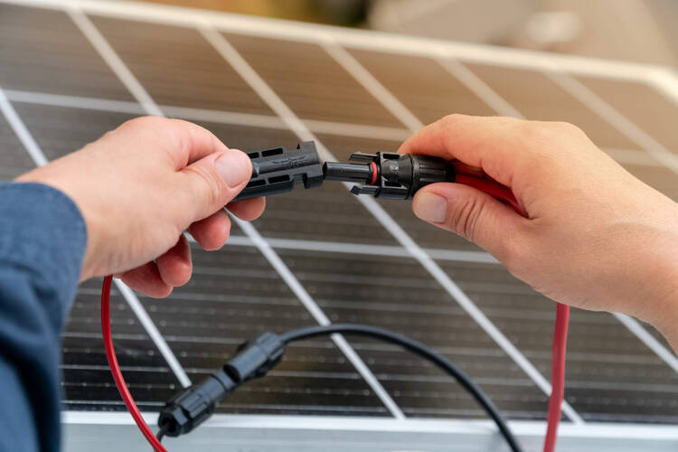 Eine Person steckt die Kabel einer Solaranlage zusammen.
