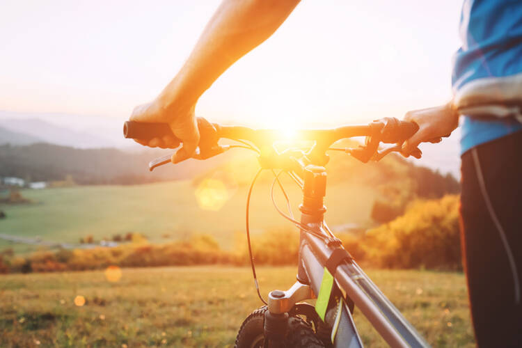 Ein Mann steht mit dem Fahrrad dem Sonnenuntergang entgegen
