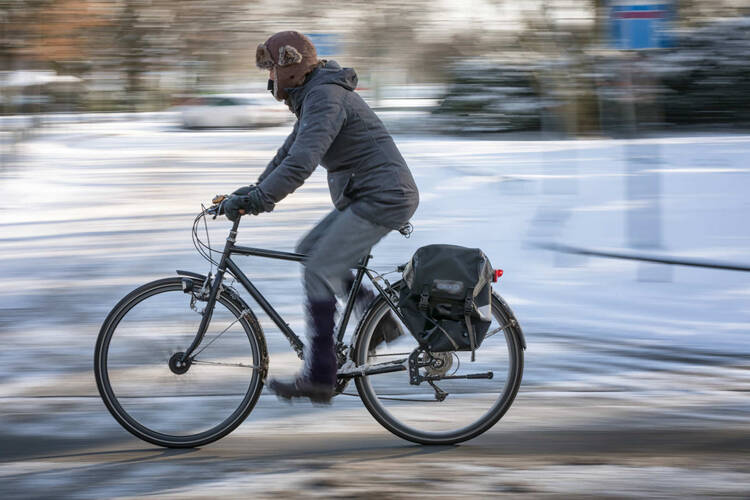 Mann fährt im Winter mit Fahrrad über verschneiten Radweg