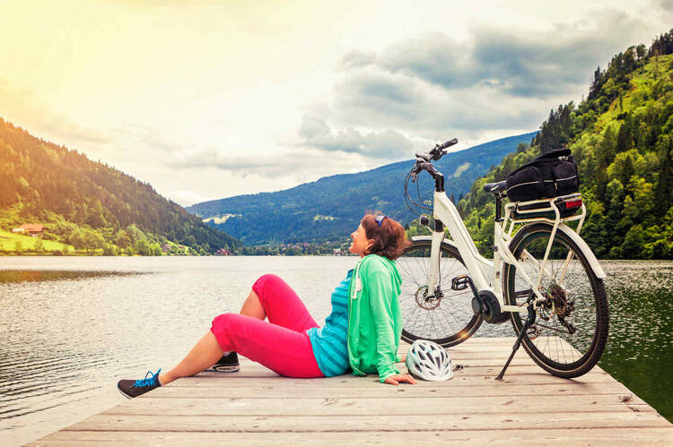 Frau sitzt neben E-Bike an See.