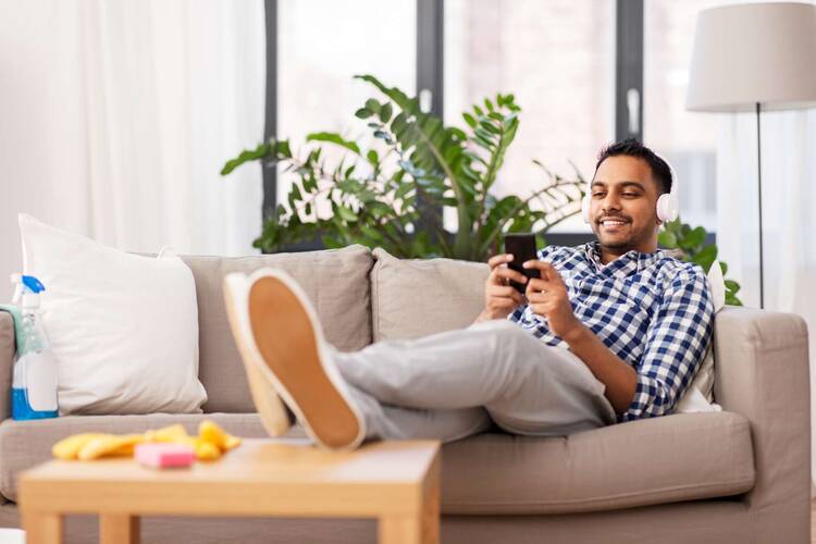 Mann sitzt lächelnd mit Kopfhörern auf dem Sofa und schaut auf sein Smartphone