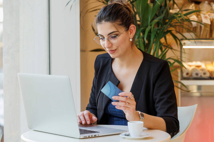 Frau sitzt am Laptop mit Kreditkarte in der Hand