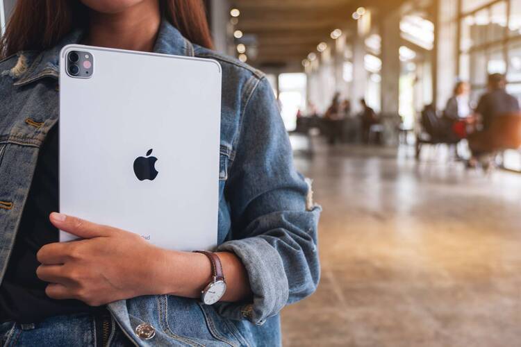 Person mit Jeansjacke hält iPad im Arm in öffentlichem Gebäude