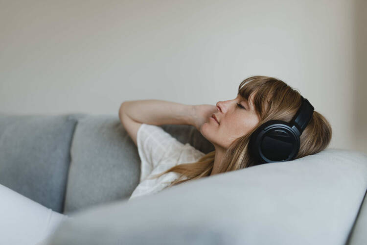 Frau liegt entspannt auf dem Sofa und hört Musik