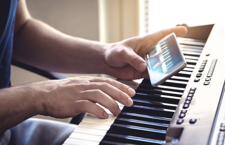 Zwi Hände an Klavier, eine Hand hält Smartphone mit Musik App