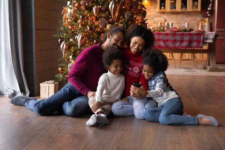Familie sitzt unter Tannenbaum und schaut lächelnd auf Smartphone