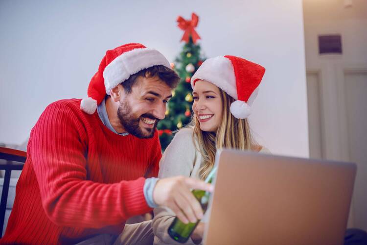 Mann und Frau mit Weihnachtsmützen sitzen fröhlich vor Laptop