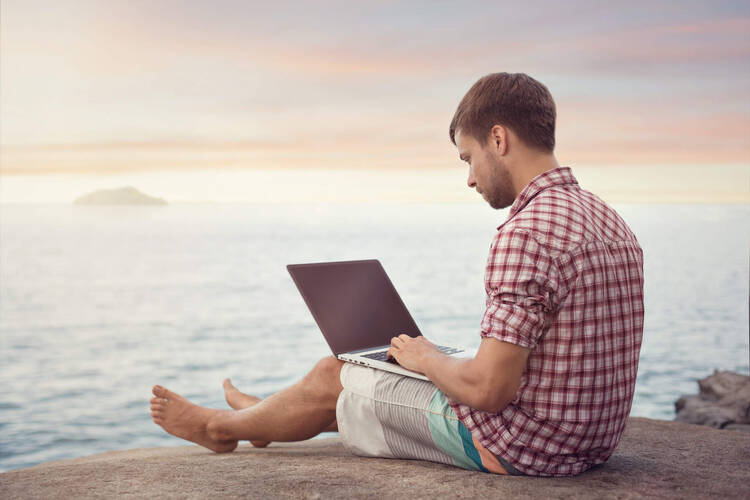 Mann sitzt am Strand mit Laptop
