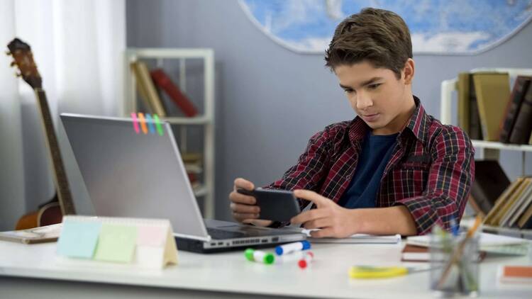 Teenager sitzt am Schreibtisch und schaut auf sein Smartphone
